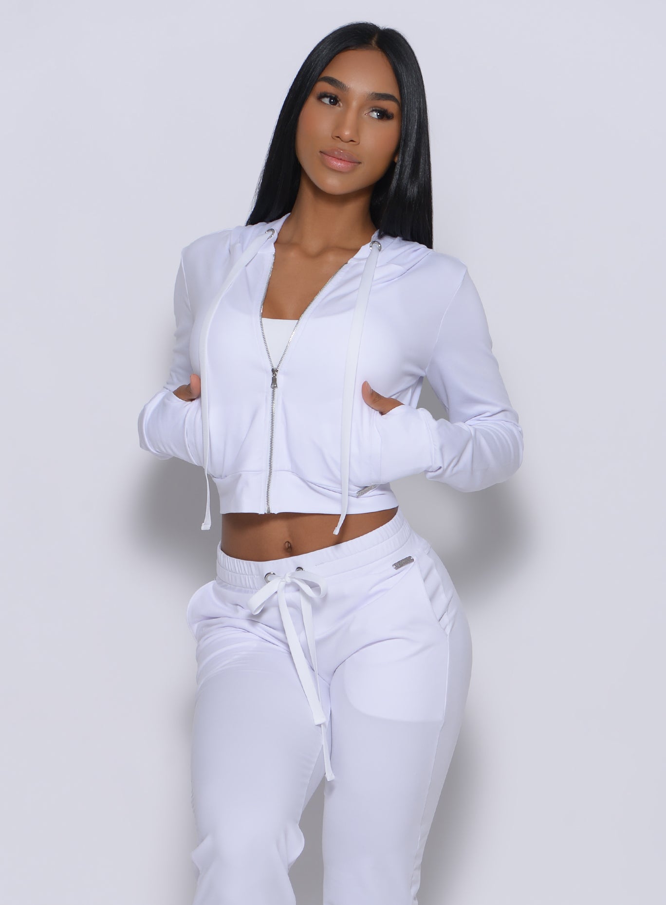 Front profile view of a model with her hands in pocket wearing our white signature jacket and a matching leggings