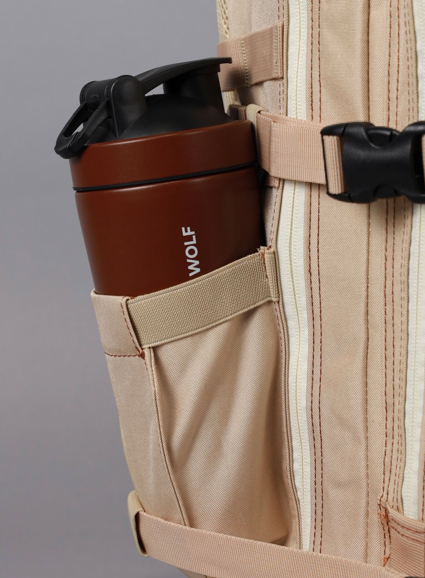 A photo showing the side of the 35L Bombshell Sportswear in latte color backpack with a bottle 