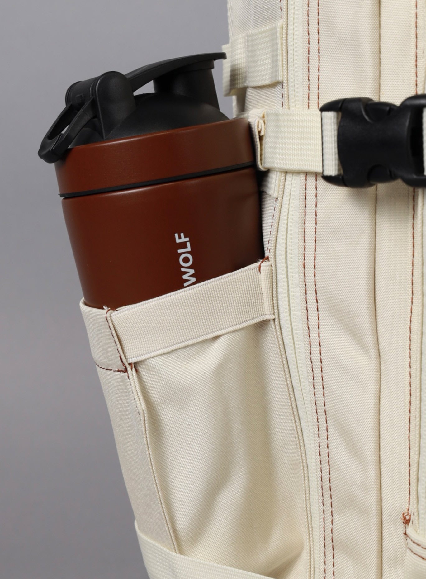 A photo showing the side of the 35L Bombshell Sportswear in  Crème color backpack with a water bottle 
