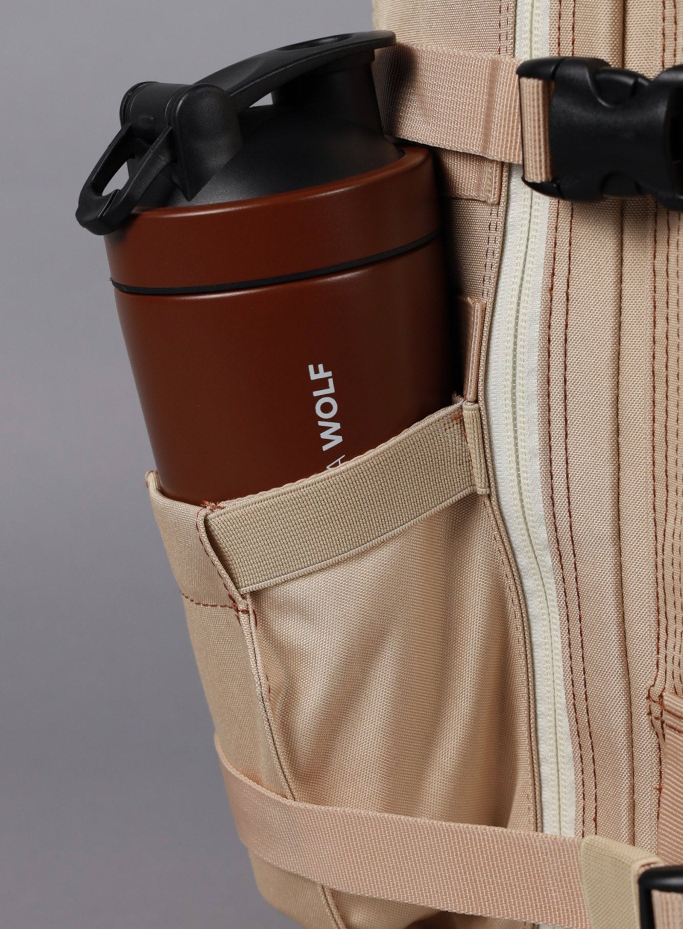 A photo showing the side of 25L Backpack Bombshell Sportswear in Latte color with a bottle 