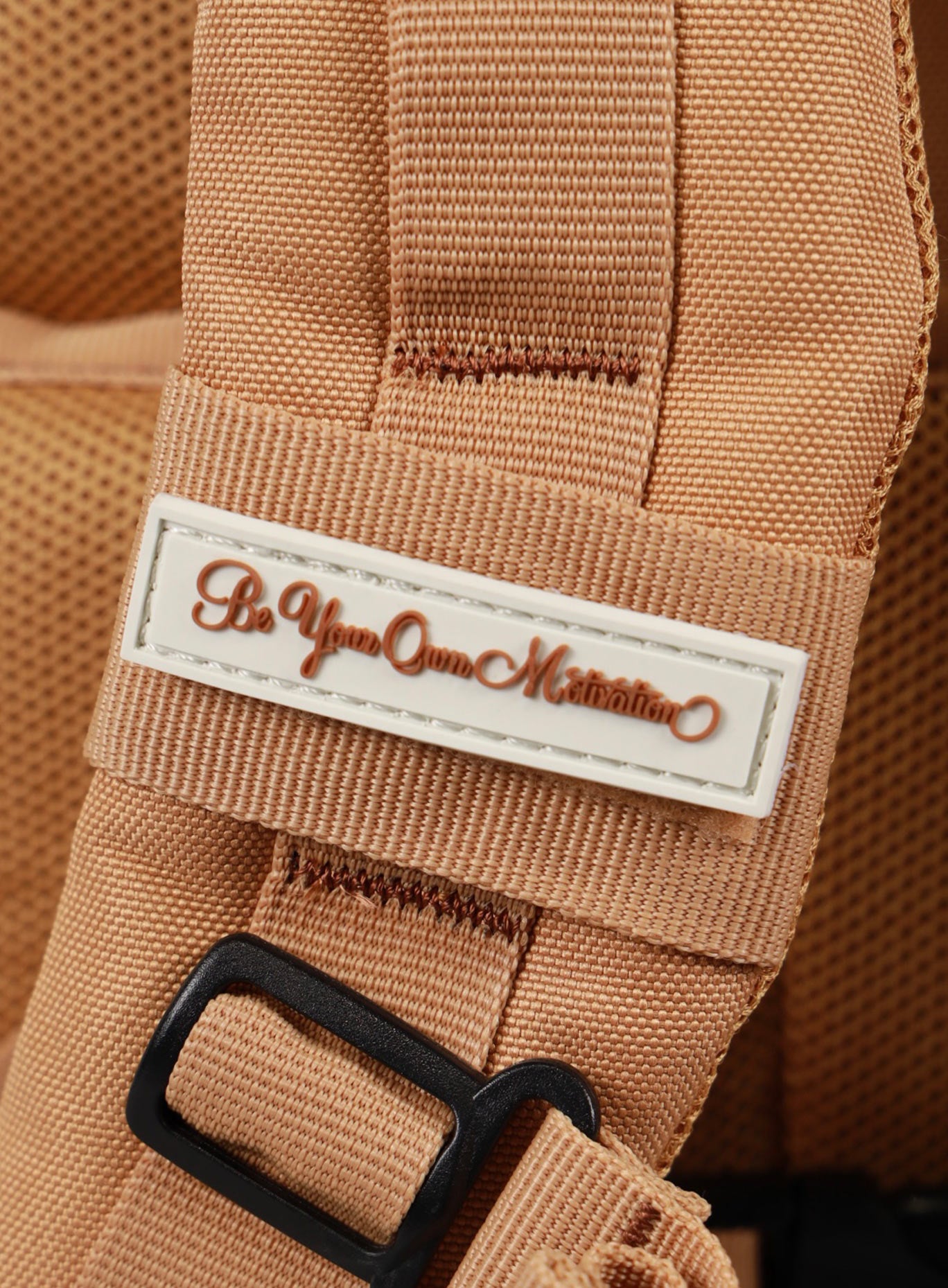 A photo depicting the be your own motivation mini patch on the strap of the 35L Bombshell Sportswear backpack in Caramel color