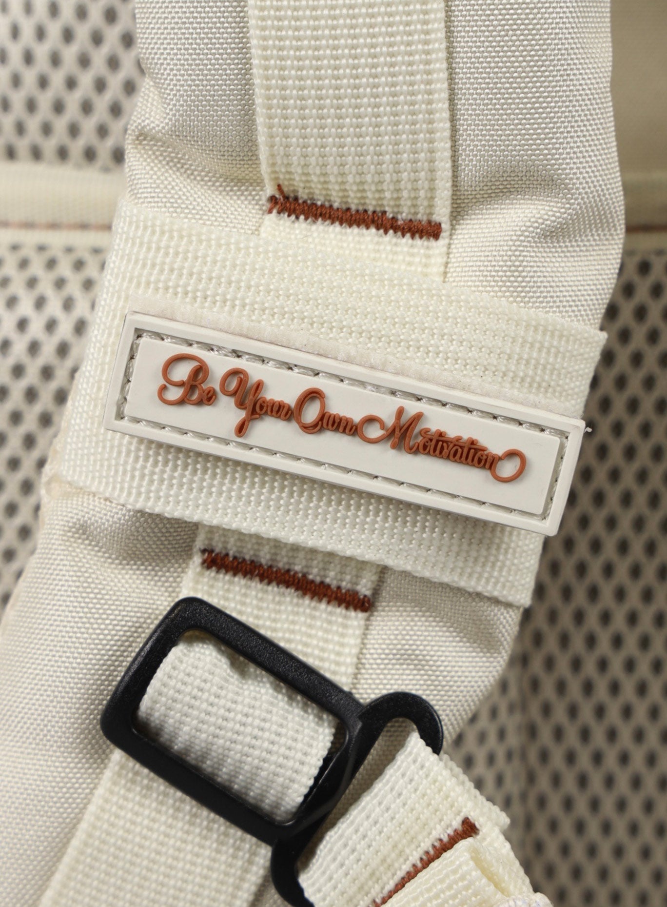 A photo depicting the be your own motivation mini patch on the strap of the 35L Bombshell Sportswear backpack in  Crème color