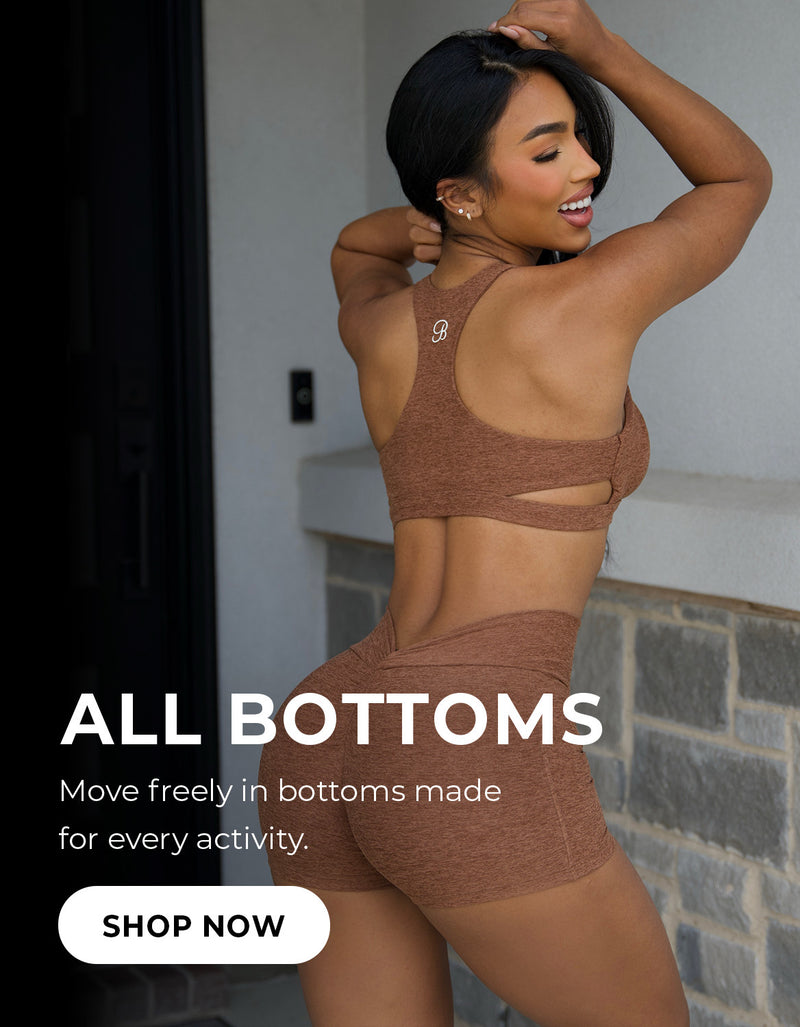 A fit model with dark hair wears a heathered brown sports bra and matching high-waisted athletic shorts. The text overlay reads 'ALL BOTTOMS – Move freely in bottoms made for every activity,' with a 'Shop Now' call-to-action button below.