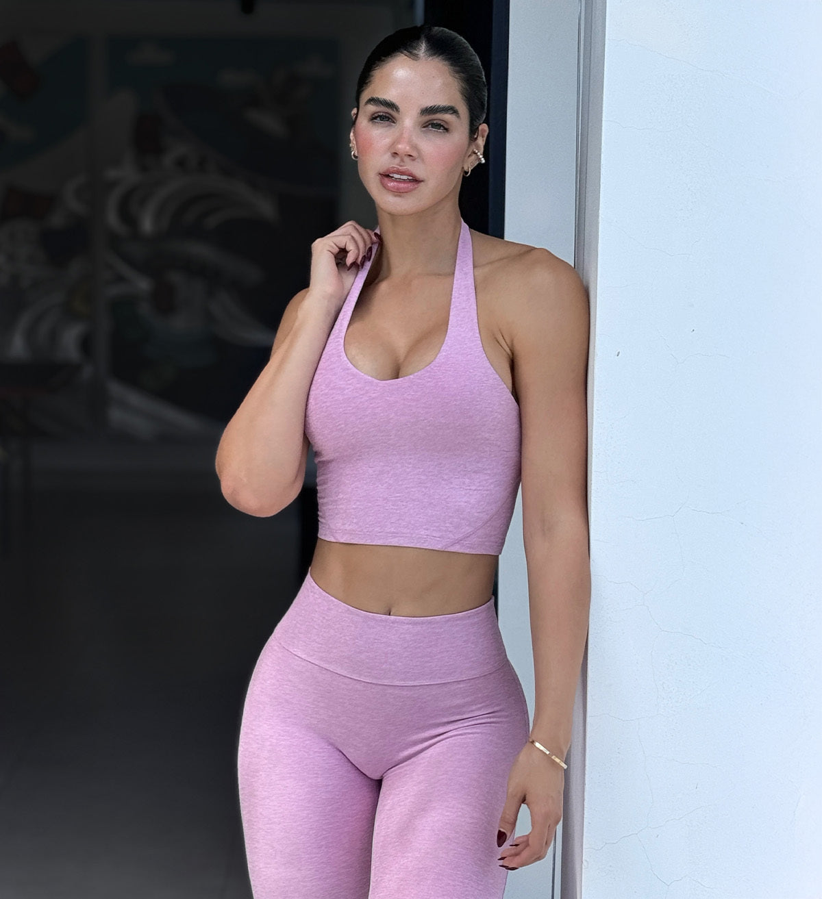 Front view of model wearing pink long bra and leggings leaning up against a white wall