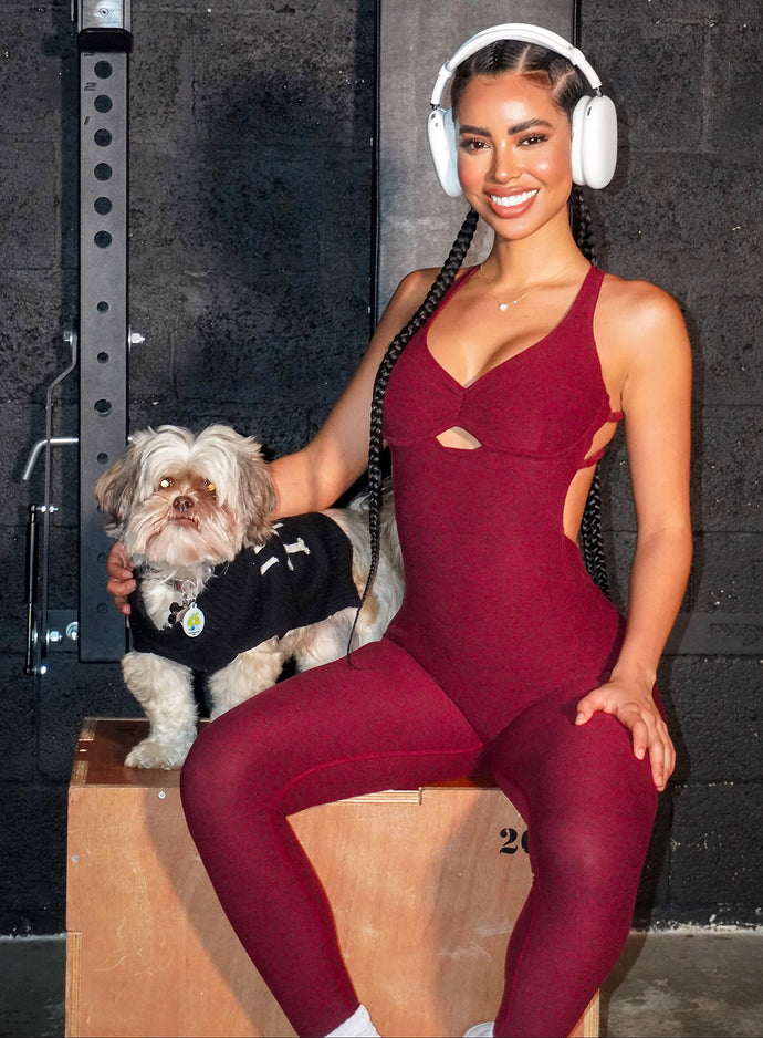 fit model sitting down on a box with her dog wearing the bombshell bodysuit in red wine