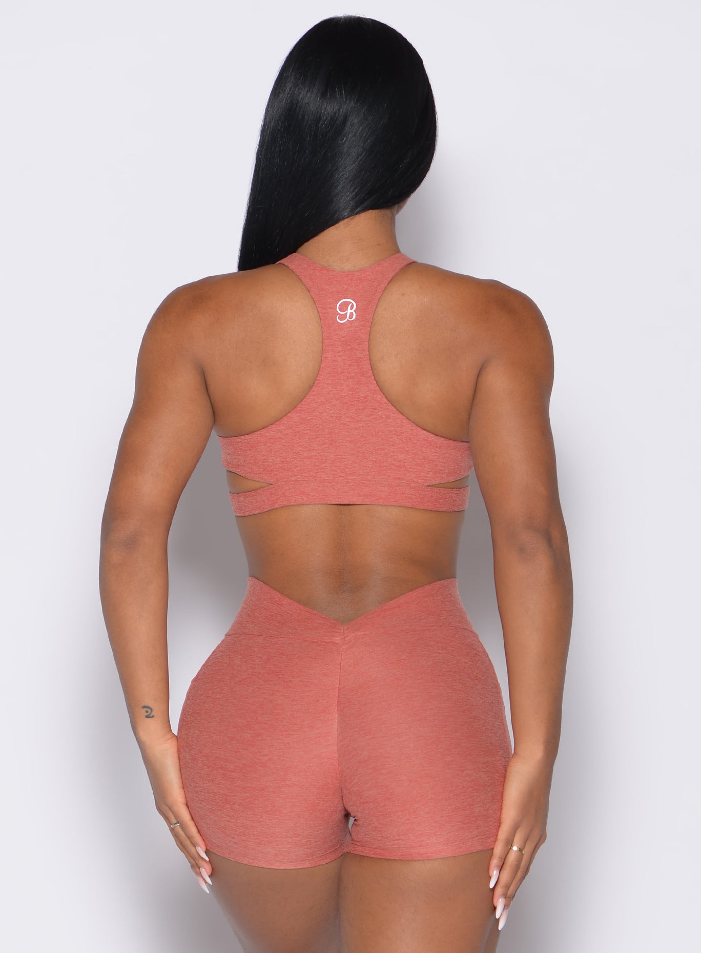 back profile view of a model with both hands on her thighs wearing the Powerhouse bra in Georgia Peach color