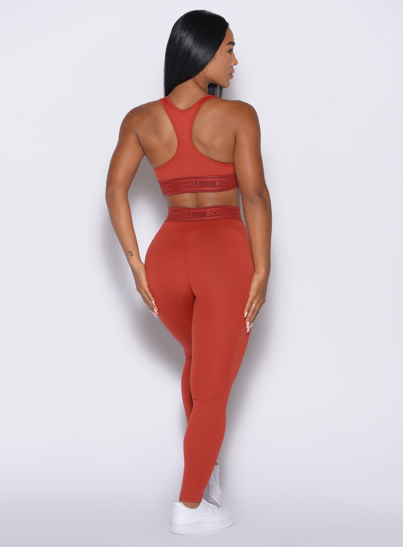 back profile view of our model with both hands resting on her thighs wearing the Bombshell Active Leggings in red ochre color