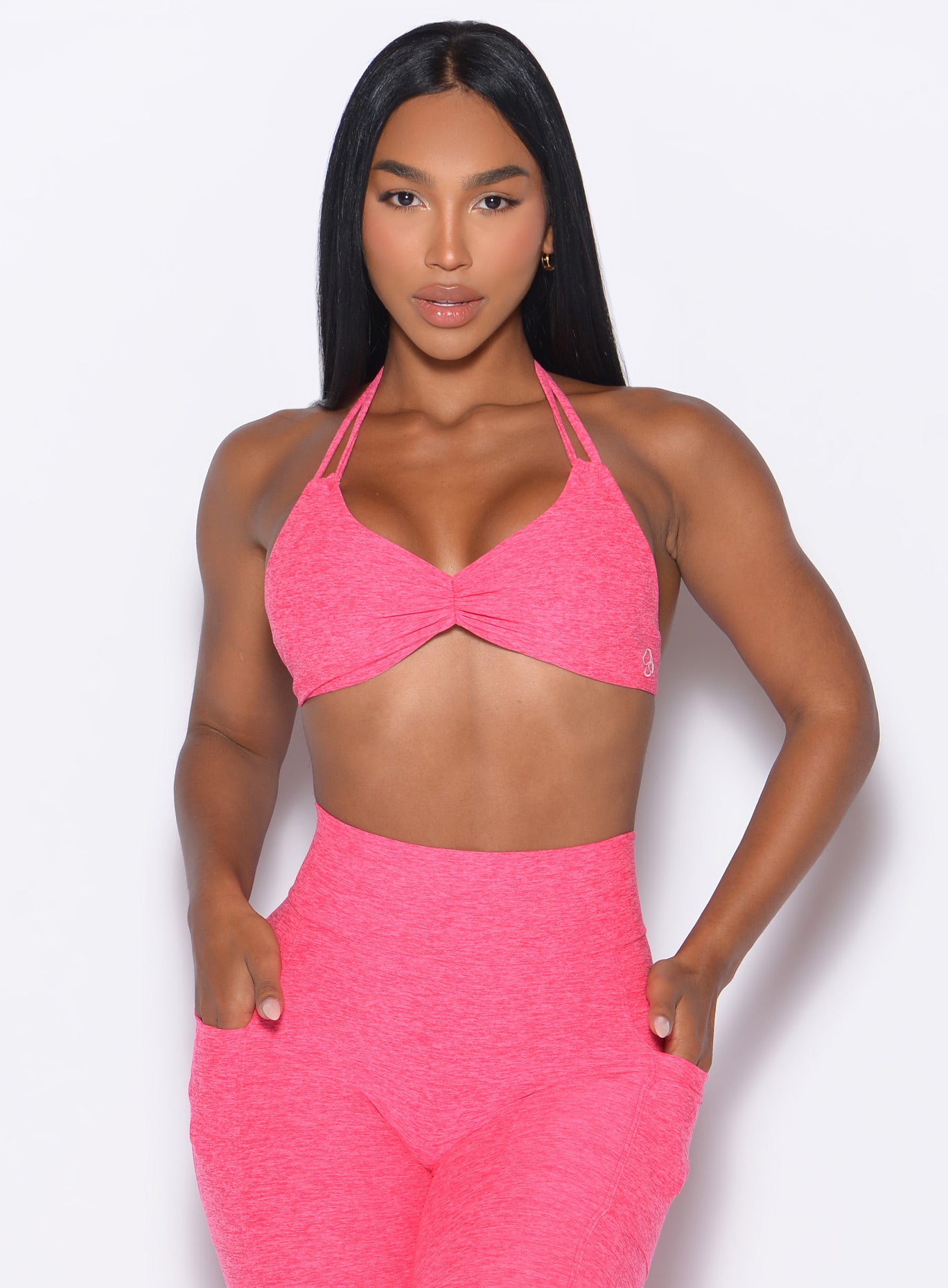 front profile view of our model with both her hands inside the pocket of the matching leggings wearing the Butterfly Sports Bra in Neon Flame color