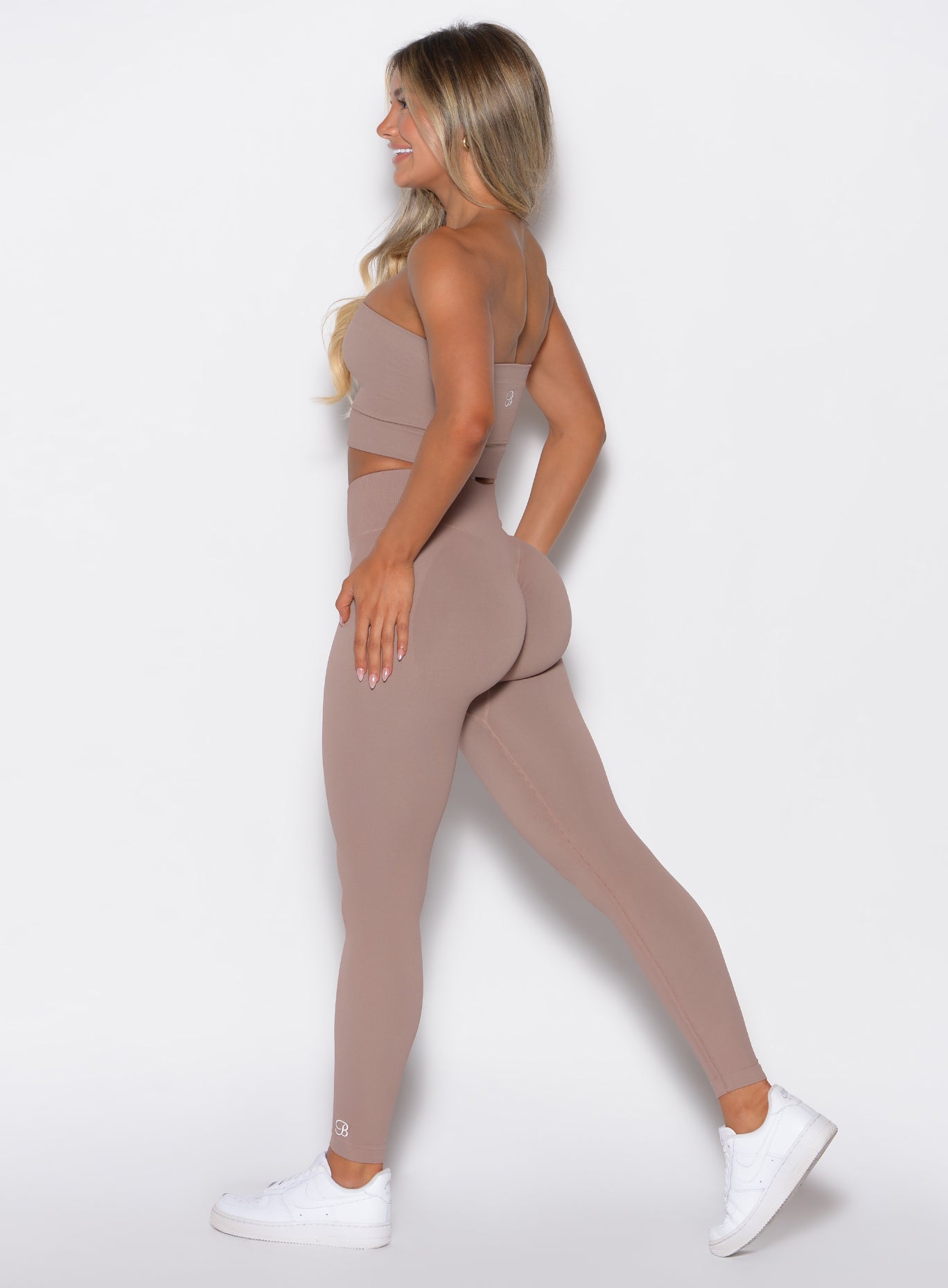 Left side profile view of a model facing forward wearing our cheeky seamless leggings in Soft Mocha color along with the matching bandeau