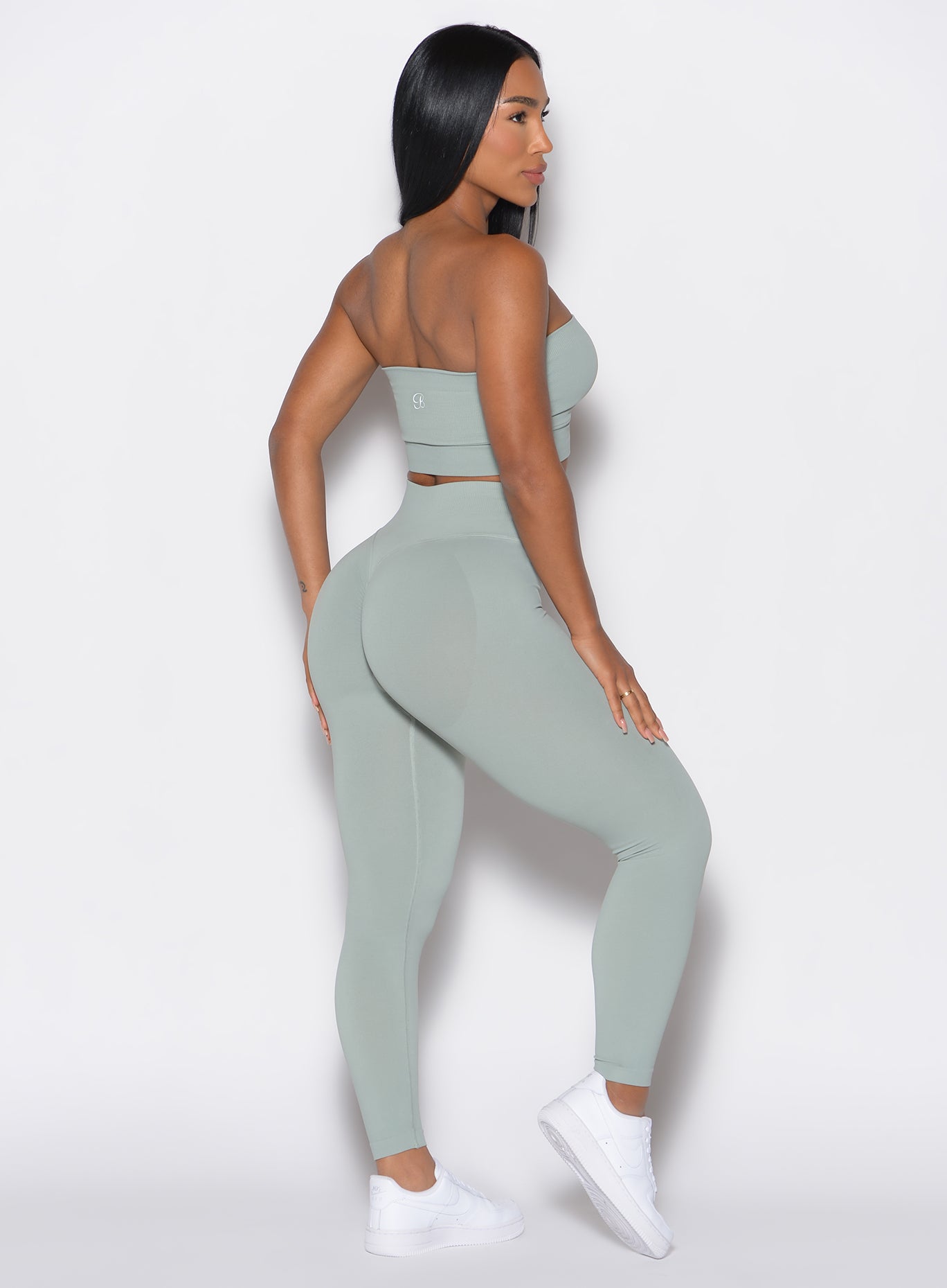 right side profile view of a model facing forward wearing our cheeky seamless leggings in light jade color along with the matching top