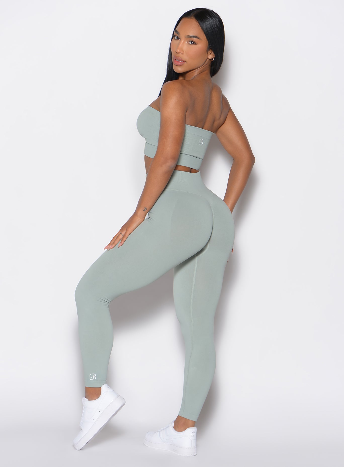 left side profile view of a model facing to her left  wearing our cheeky seamless leggings in light jade color along with the matching top