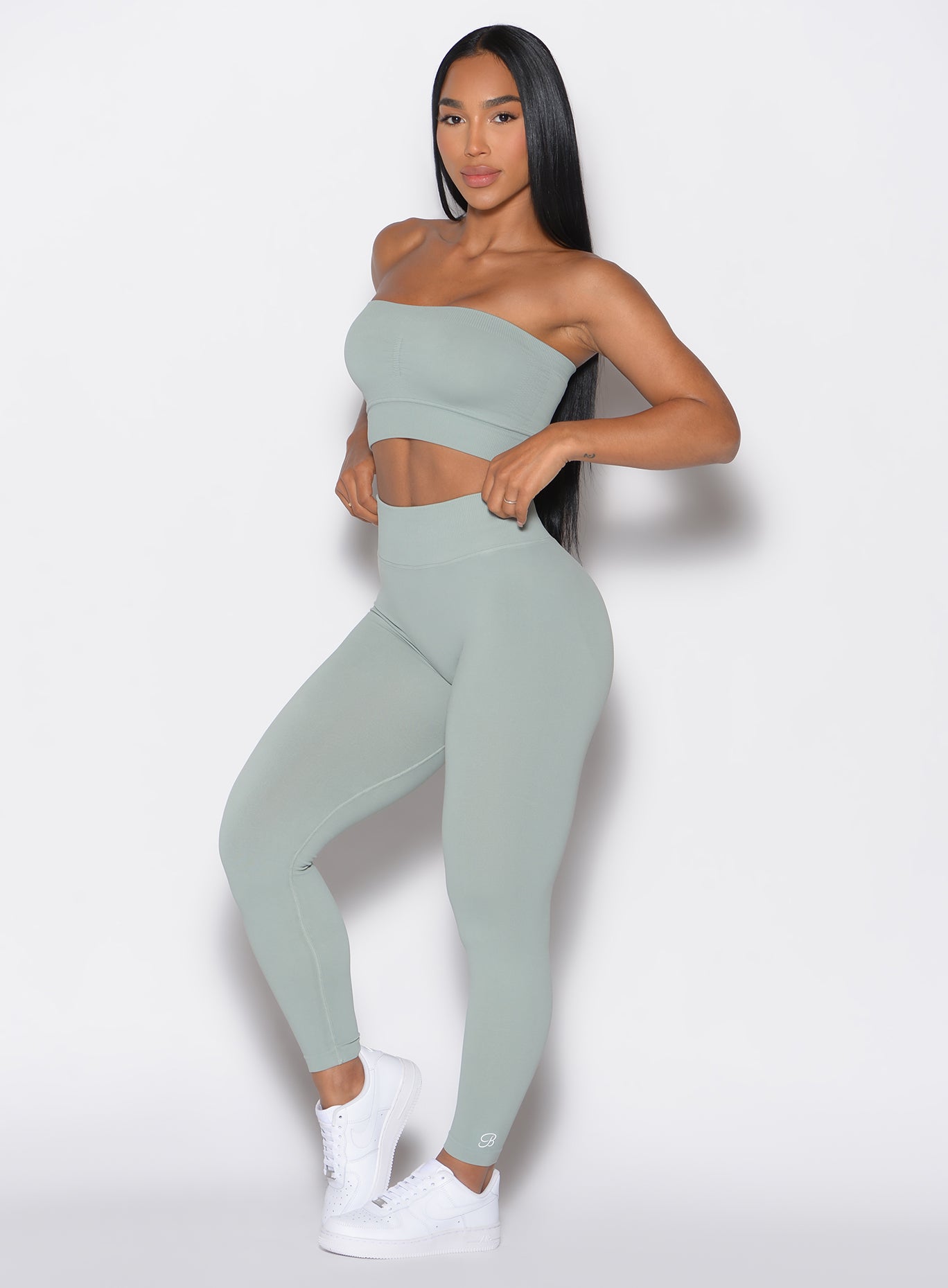front profile view of a model adjusting her waistband of the  cheeky seamless leggings that she is wearing in light jade color along with the matching top