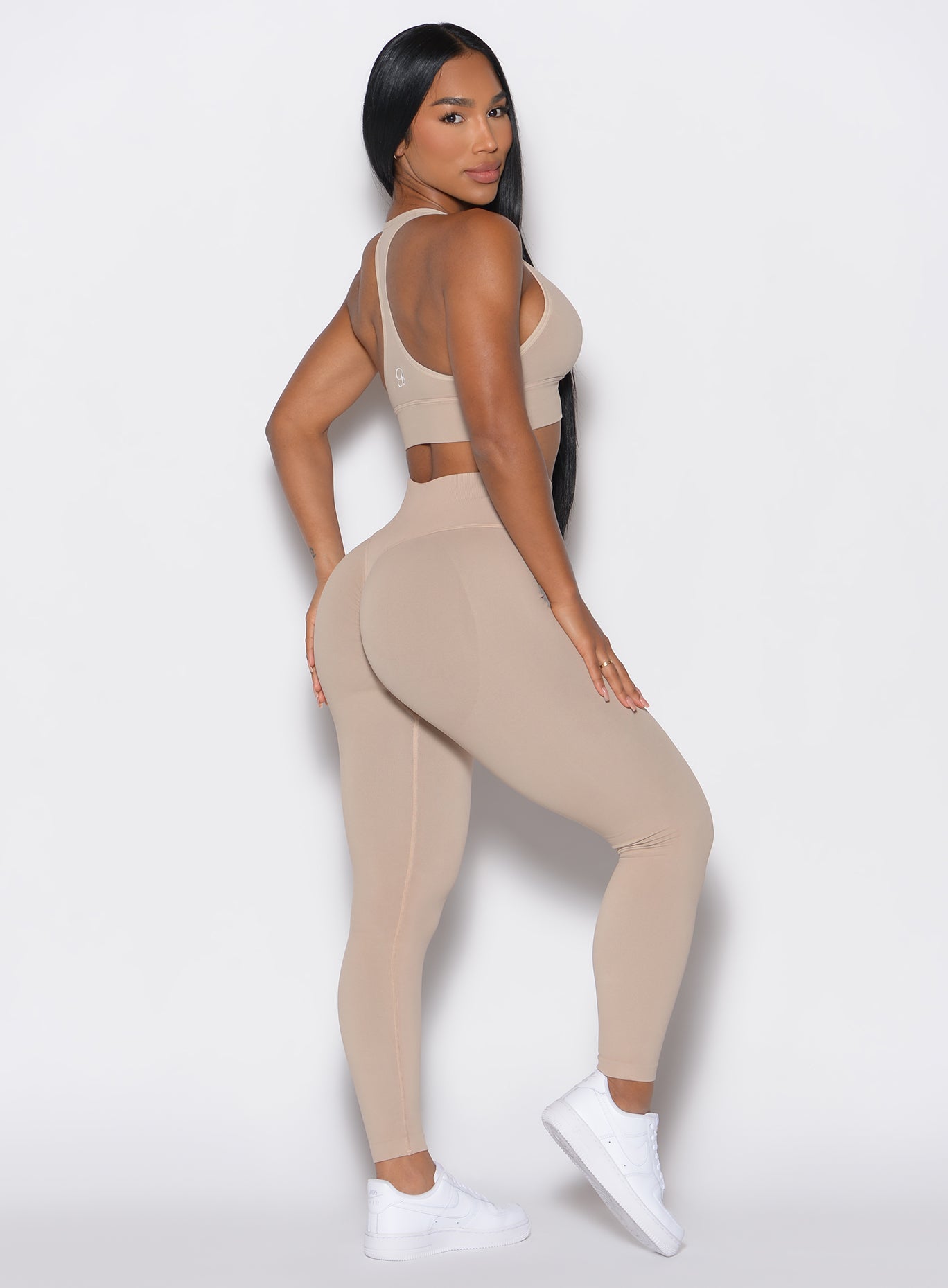 right side profile view of a model facing to her right wearing our cheeky seamless leggings in Timeless Taupe color along with the matching sports bra