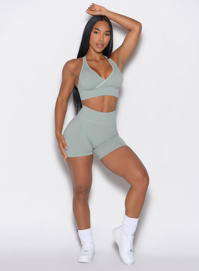 front profile view of a model with her hands over her head wearing our cheeky seamless shorts in soft mocha color along with a matching sports bra