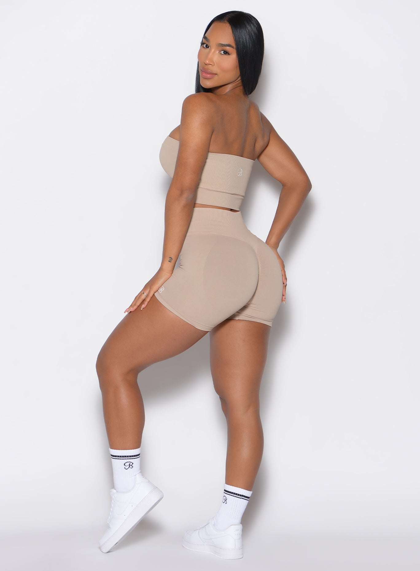left side profile view of a model facing to her left wearing our cheeky seamless shorts in timeless taupe color along with a matching bandeau