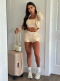 Front profile shot of our model wearing our Cloud Crop Jacket in vanilla color with matching shorts and top and a suitcase to her right side. 