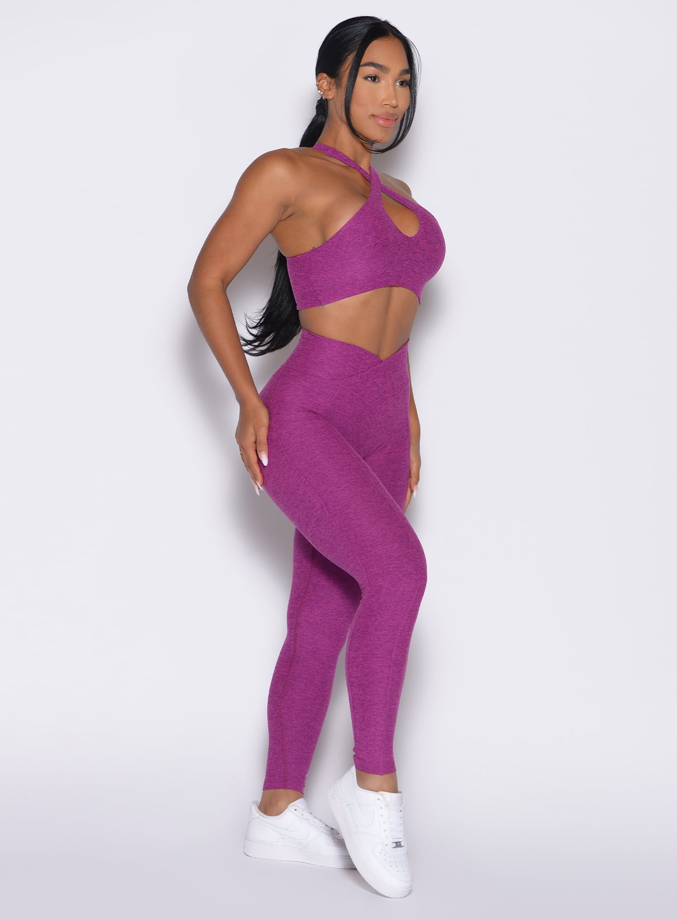 Right side profile view of a model angled right wearing our Contour Leggings and the matching Cross Over Halter Bra in Bright Plum color
