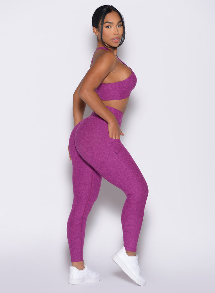 Right side view of a model facing to her right wearing our Contour Leggings and the matching Cross Over Halter Bra in Bright Plum color