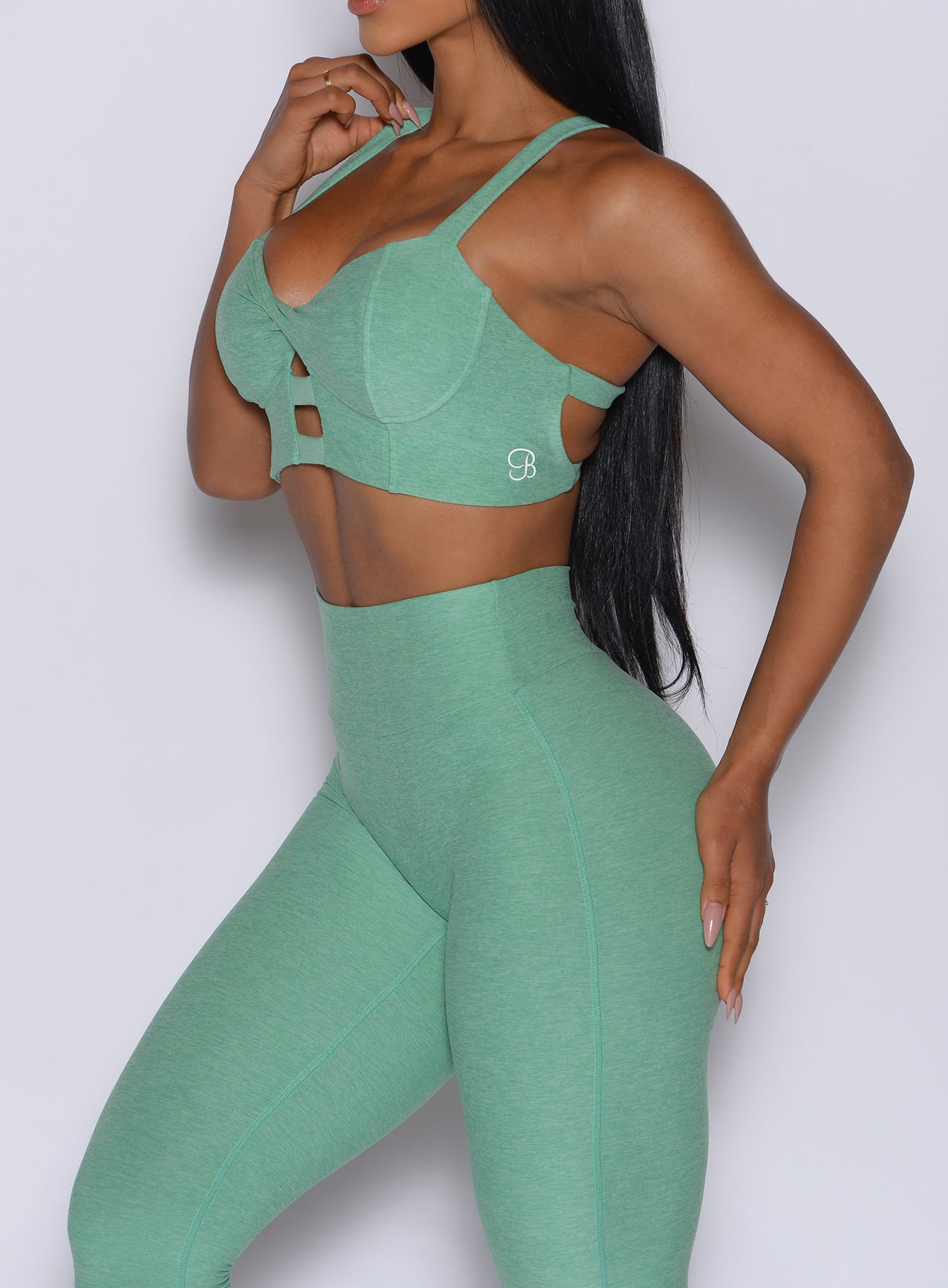left side profile view of a model wearing our core set bra in sage color along with the matching leggings