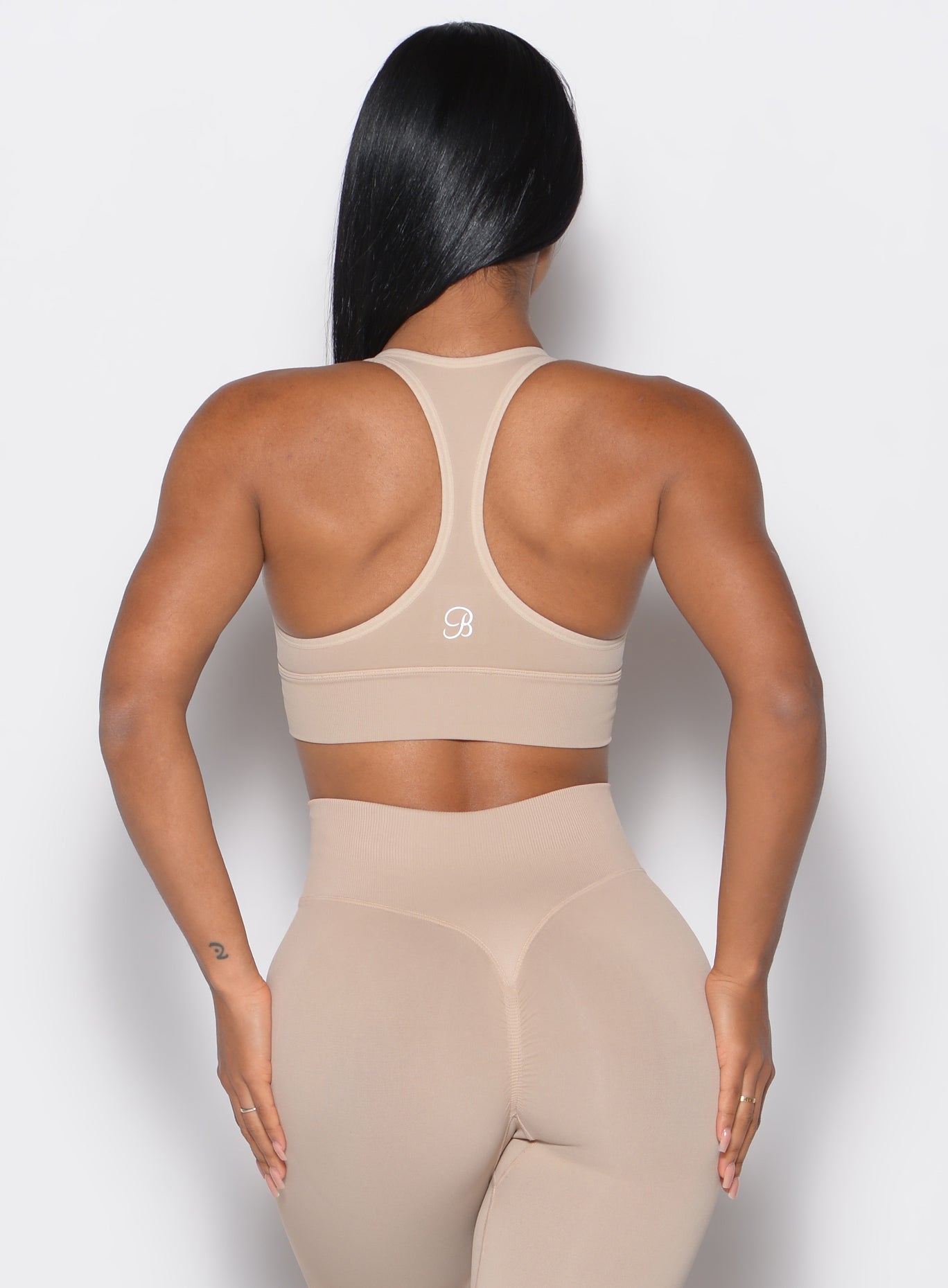 back  profile view of a model wearing our cross over bra in timeless taupe color along with the matching leggings