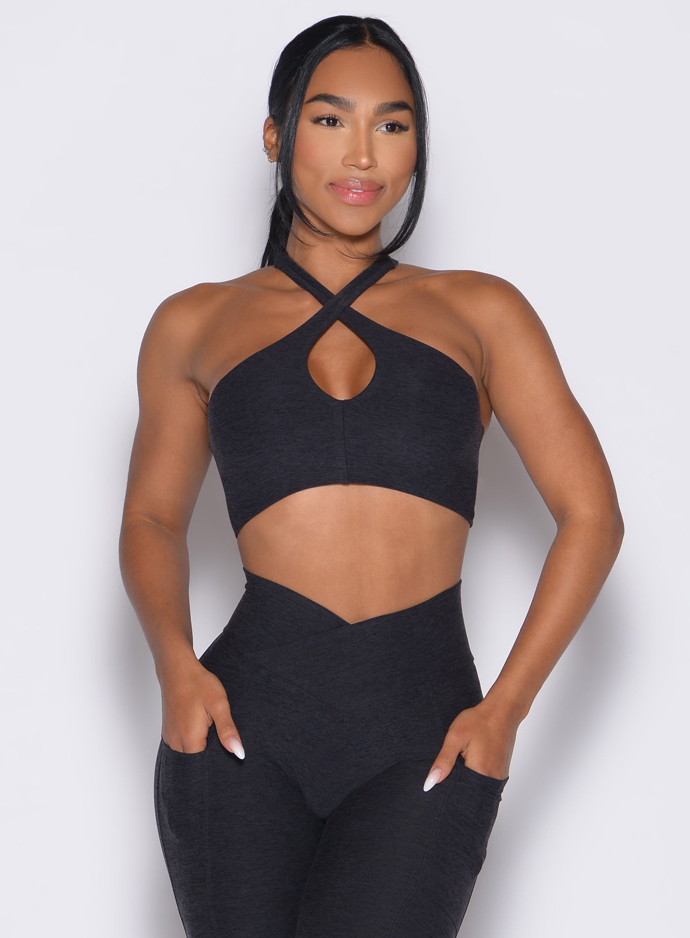 front profile view of a model wearing our Cross Over Halter Bra and the matching leggings in Heathered Black color