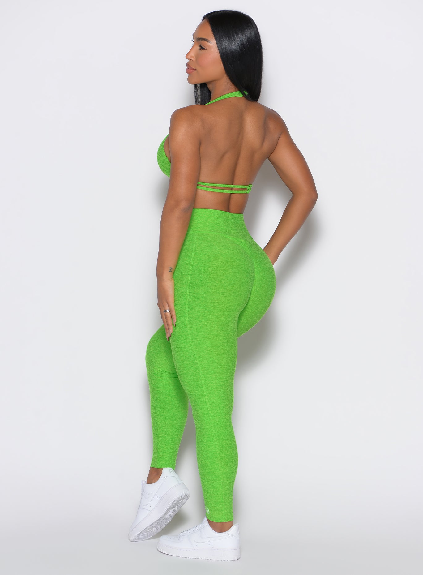 left side profile view of a model facing to her left wearing our curves leggings in Neon Lime Green color along with the matching sports bra