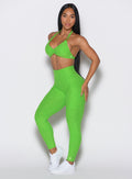 left side profile view of a model angled slightly to her left  wearing our curves leggings in Neon Lime Green color along with the matching sports bra