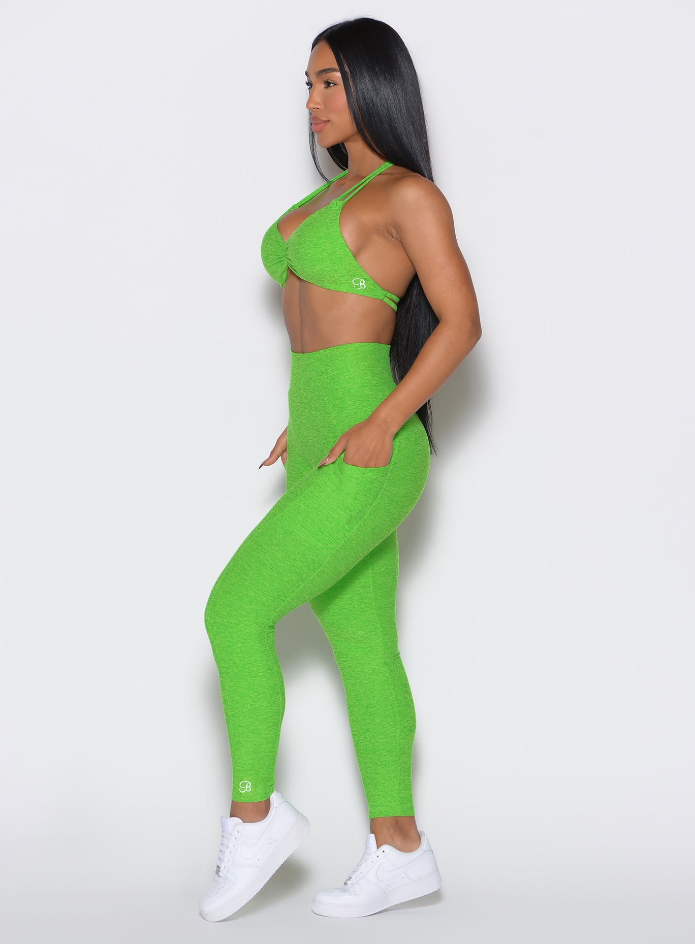 left side profile view of a model facing forward wearing our curves leggings in Neon Lime Green color along with the matching sports bra