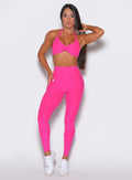 Front profile view of a model wearing our curves leggings in Neon Pink Berry color along with the matching bra 