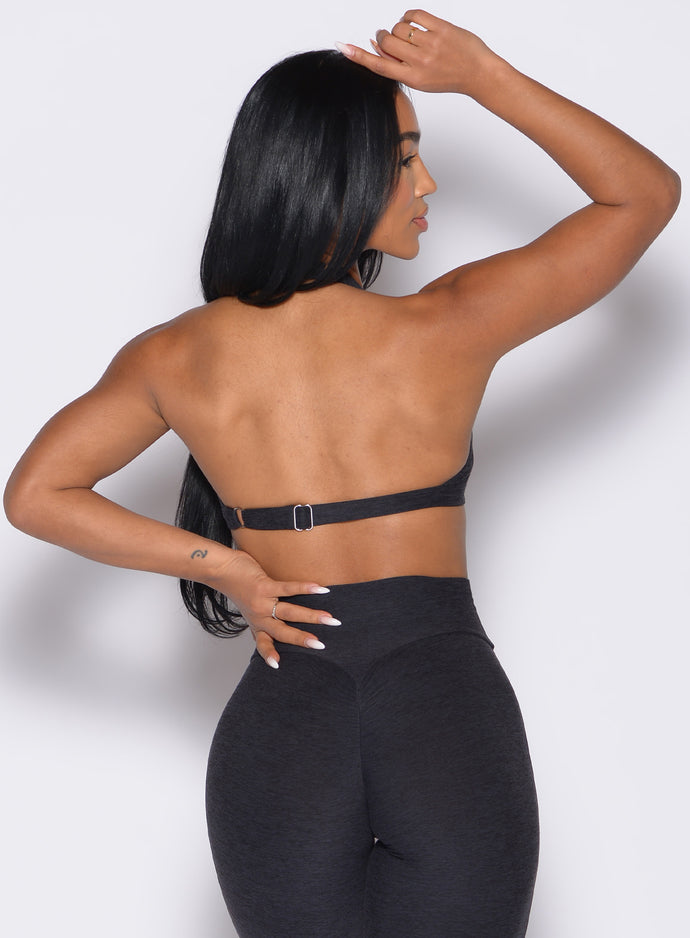 back profile view of a model with one hand placed on her forehead and the other on her waist wearing the Iron Edge Bra in Heathered Black color