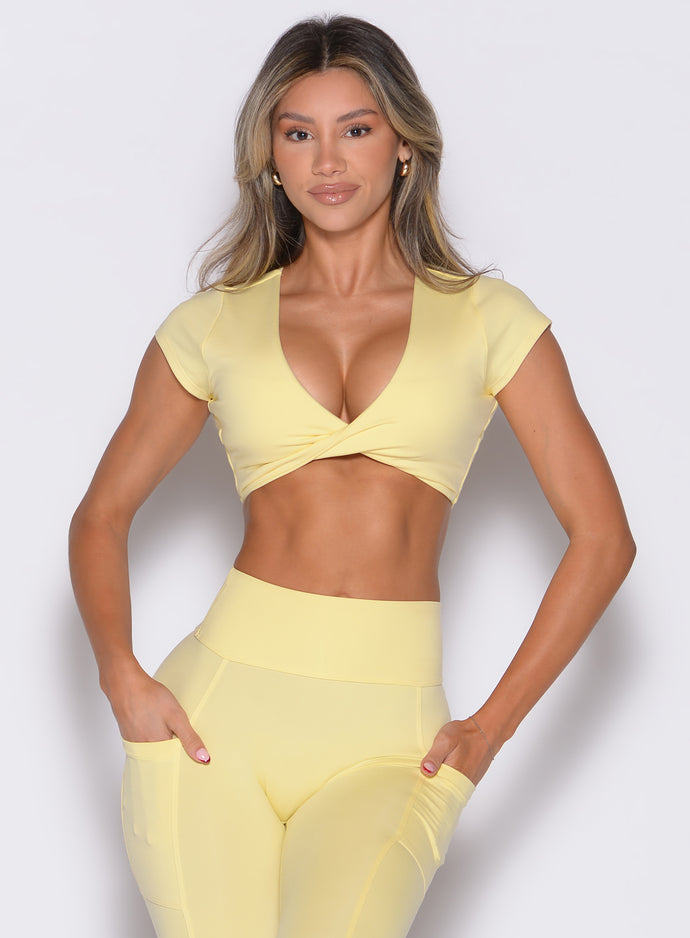 front profile view of a model with both hands inside the pockets of the leggings wearing the Fab Bust Bra in soft yellow color