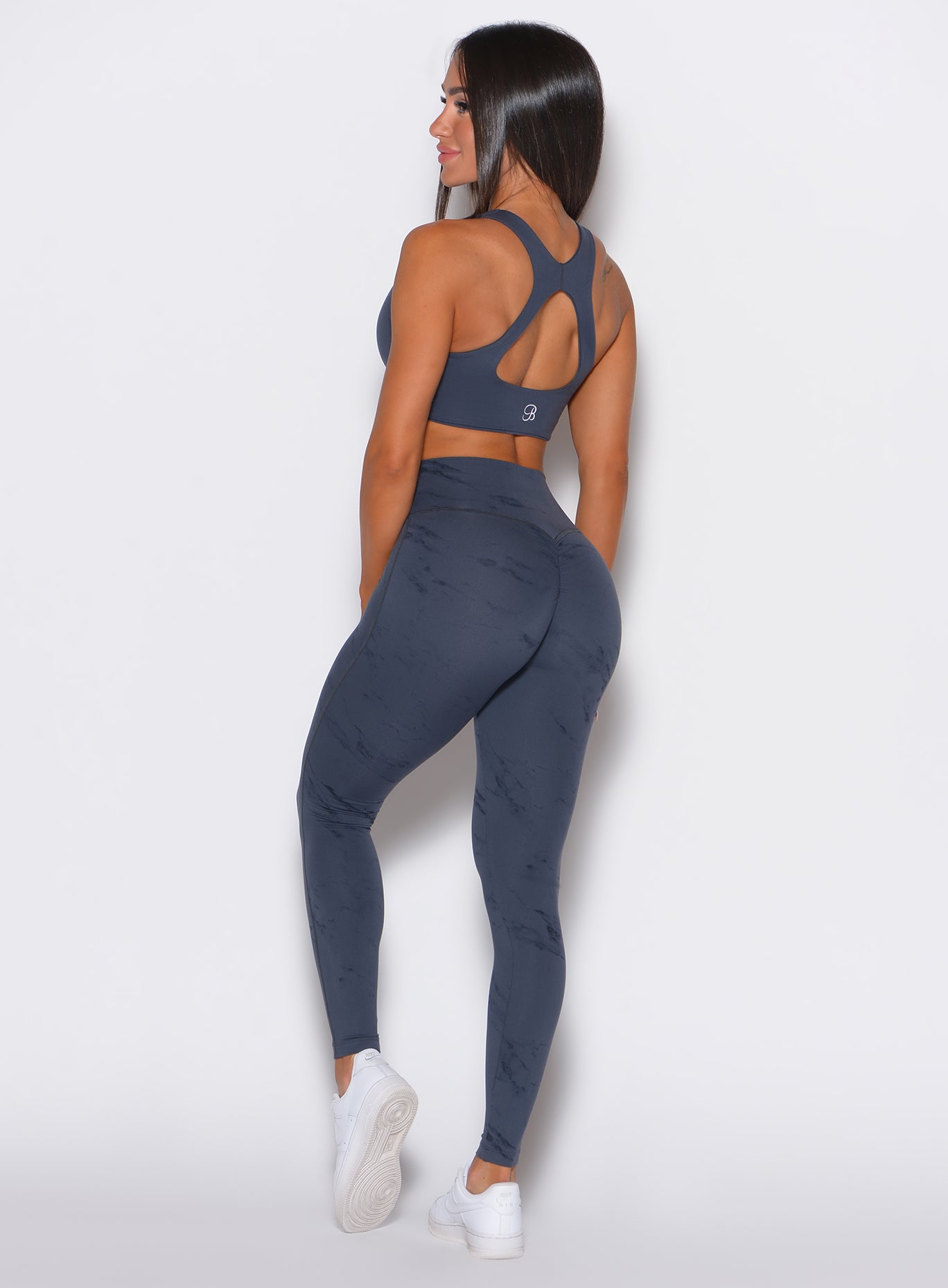 left side profile view of a model facing to her left wearing our fit marble leggings in thunder gray color along with a matching bra