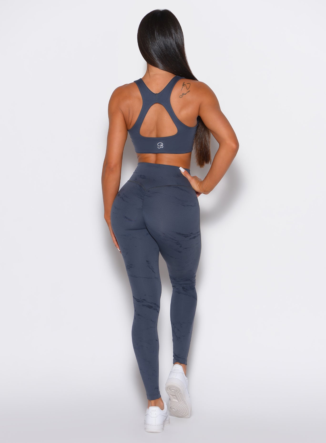 back profile view of a model wearing our fit marble leggings in thunder gray color along with a matching sports bra