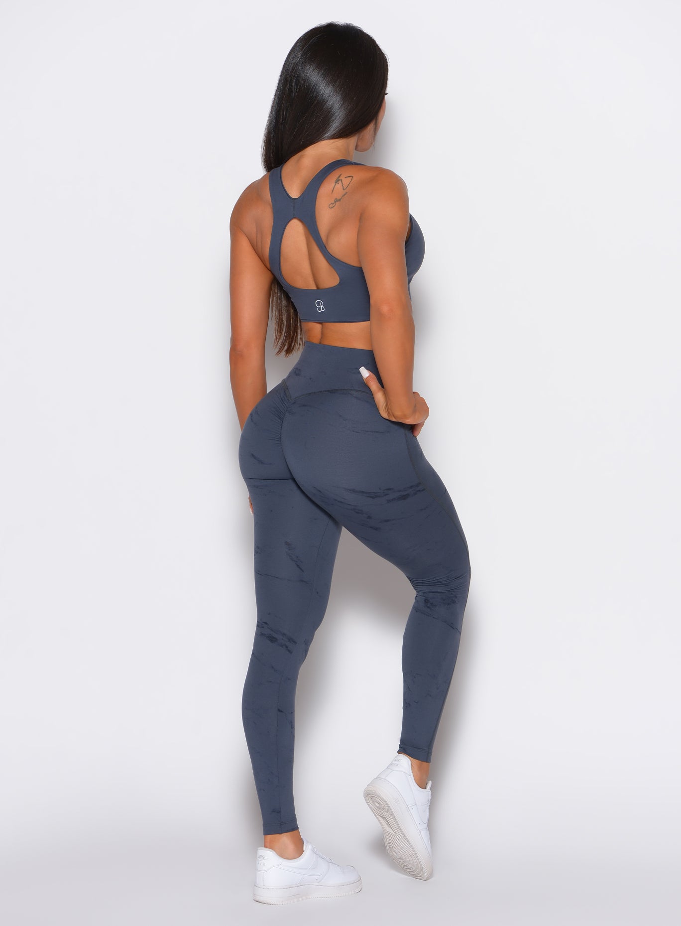 back profile view of a model wearing our fit marble leggings in thunder gray color along with a matching bra