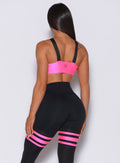 Back profile view of a model in our glow sports bra in neon pink and a matching thigh high leggings