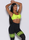 Front profile view of a model with her hands over her head wearing our glow sports bra in neon yellow and a matching thigh high