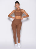 front profile view of a model with both hands on the waistband wearing the V Butt Lift Leggings in Coffee Bean color