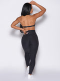 back profile view of a model with one hand on her waist wearing the Movement Leggings in Heathered Black color