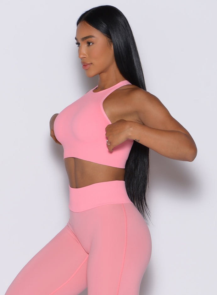 left side profile view of a model facing forward wearing our Lifter Seamless Bra and the matching leggings in Peach Burst color