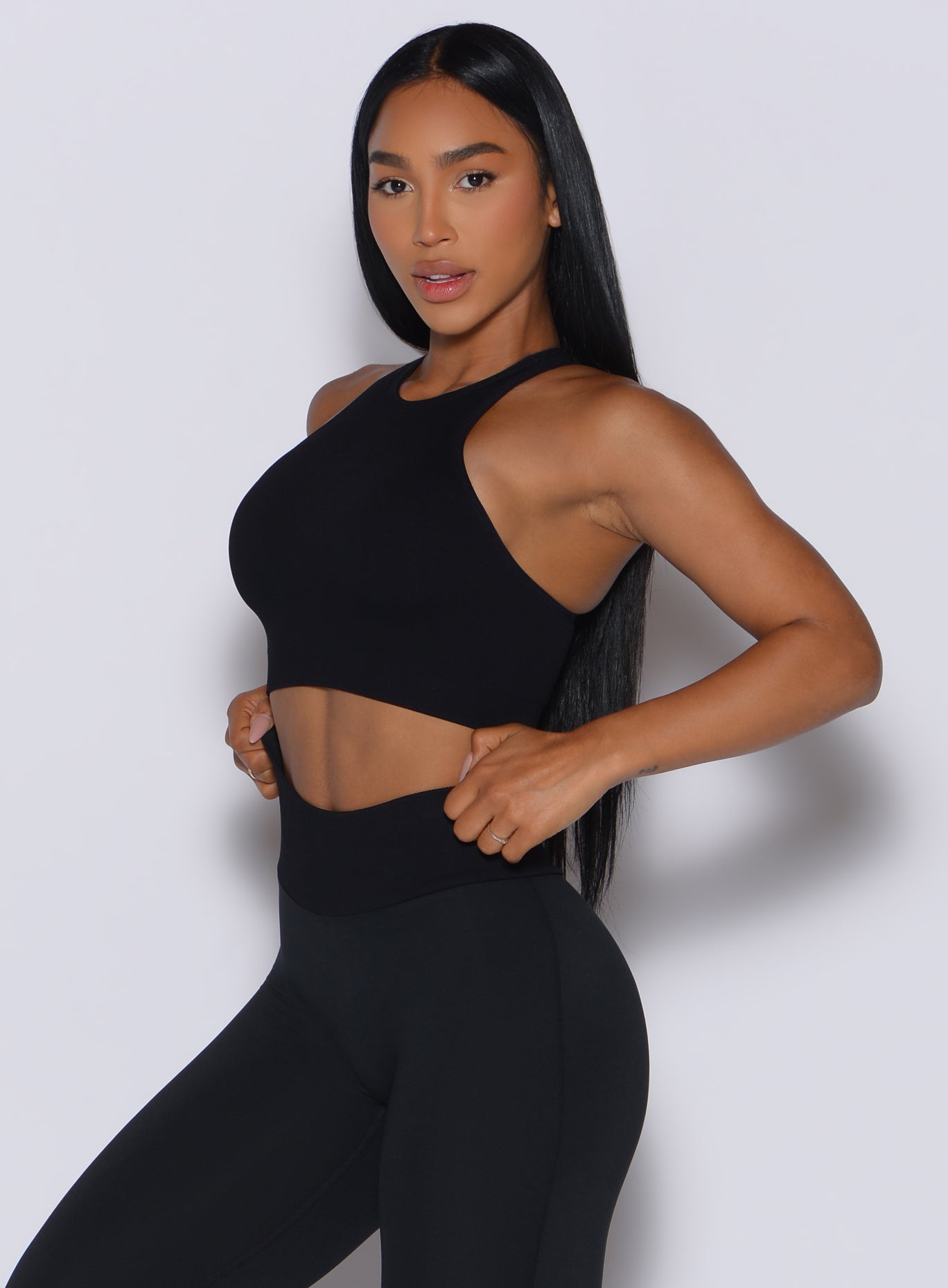 Front left side profile view of our model adjusting the waistband of the leggings wearing our Lifter Seamless Bra in Black color