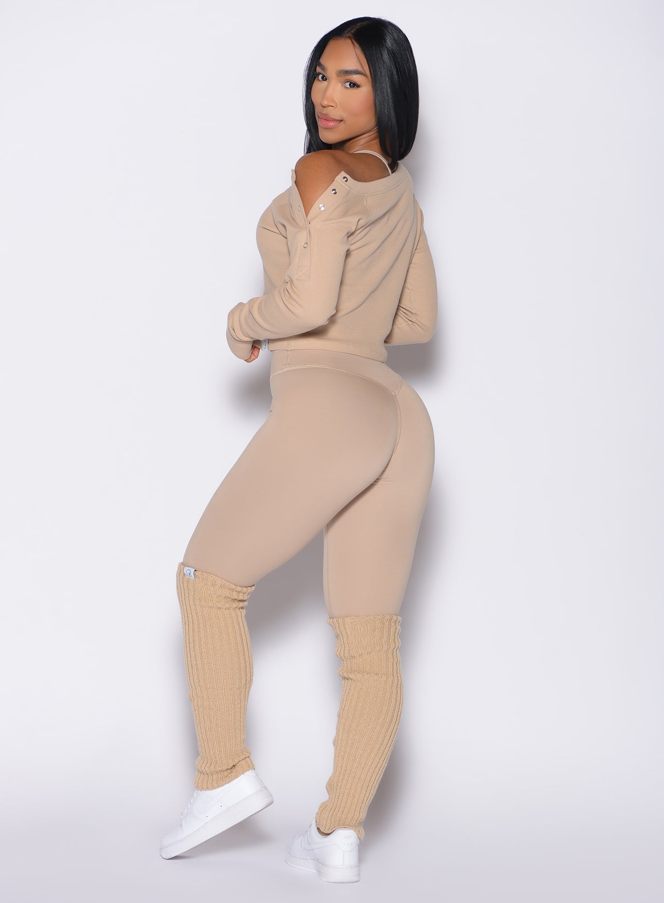 left side profile view of a model looking over her shoulder wearing the Internal Scrunch Leggings in Glacial beige color paired with the matching pullover 