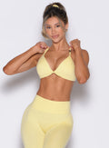 front profile view of a model with both hands on the strap of the bra wearing the Kini Bra in soft yellow color