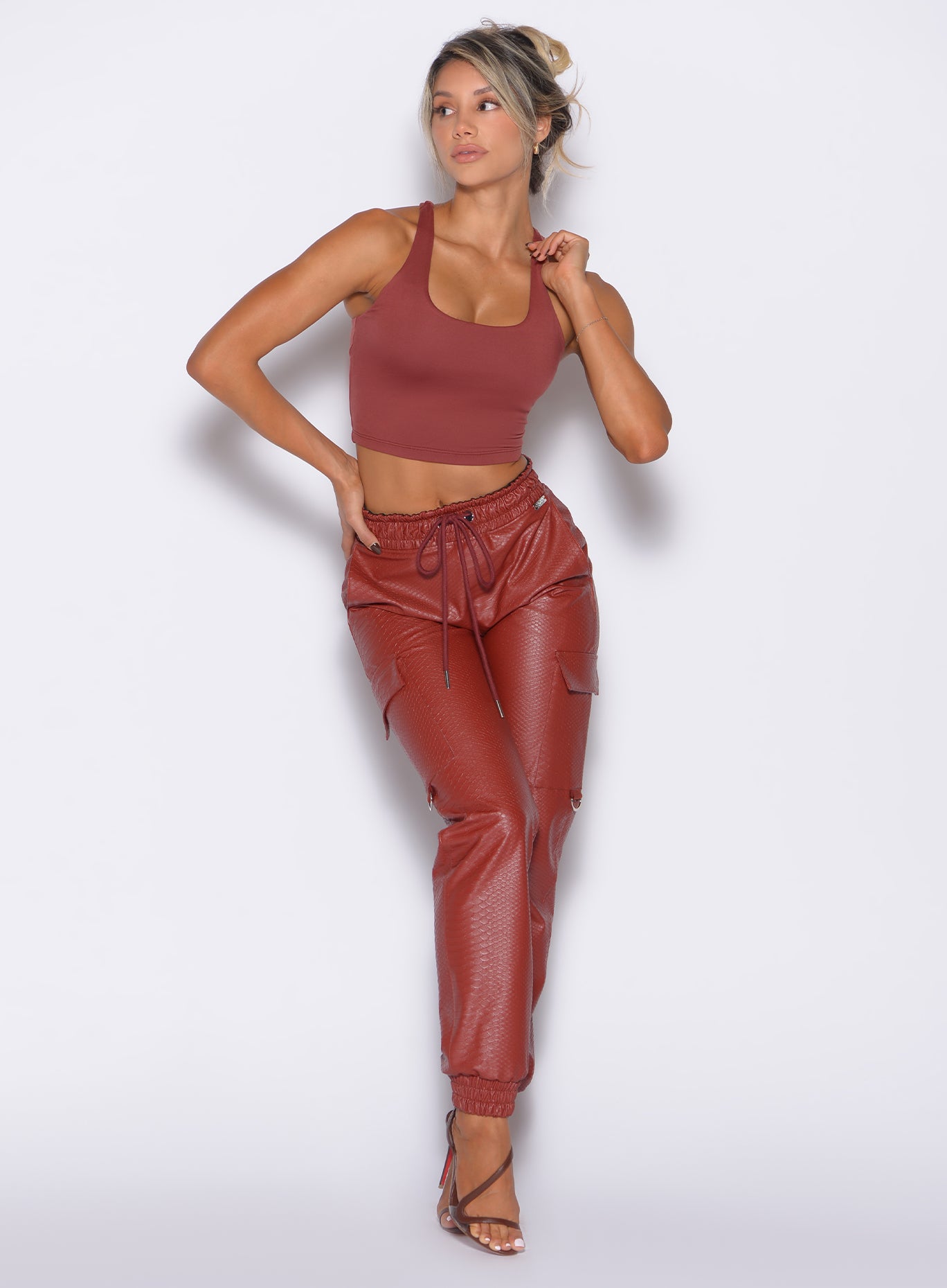 front profile view of our model with one hand on her waist and the other on the strap of the tank wearing the Liquid Cargos in brick red color