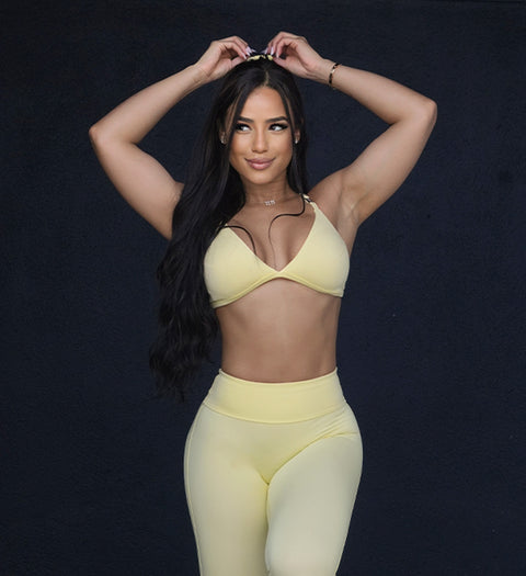 front view image of model tightening her hair scrunchie wearing the kini bra and matching leggings in yellow.