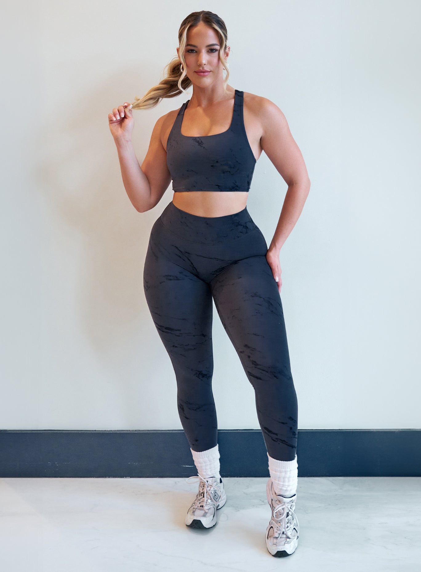 front profile view of a model facing forward wearing our fit marble leggings in thunder gray color along with a matching bra