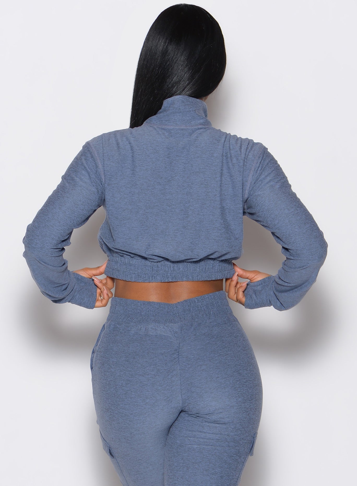 Back profile view of our model wearing the Cloud Crop Jacket in twilight color with both her hands on the band of the jacket