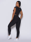 back profile of model angled left wearing the Movement Leggings in Onyx  color and a matching Tee