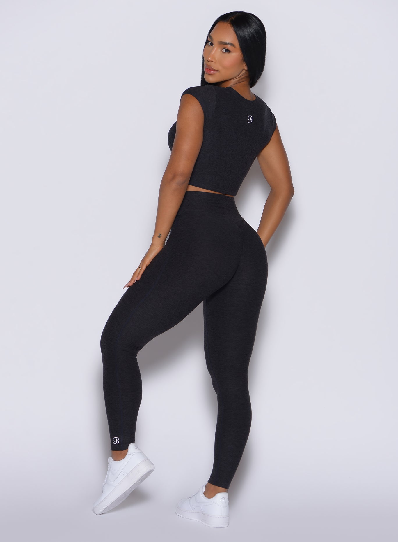 back profile of model angled left wearing the Movement Leggings in Onyx  color and a matching Tee