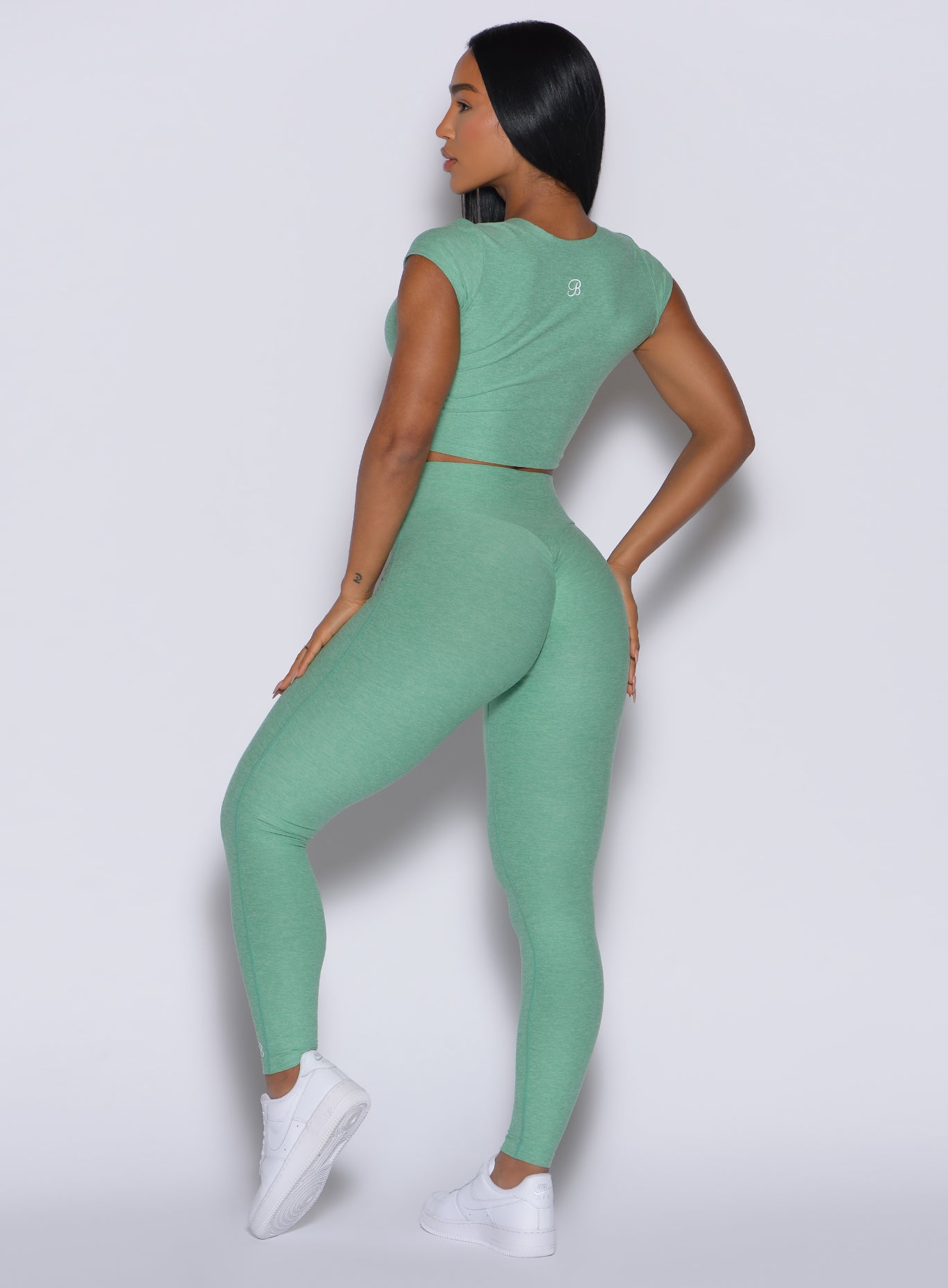back profile view of model facing to her left wearing the Movement Leggings in Sage color and a matching Tee