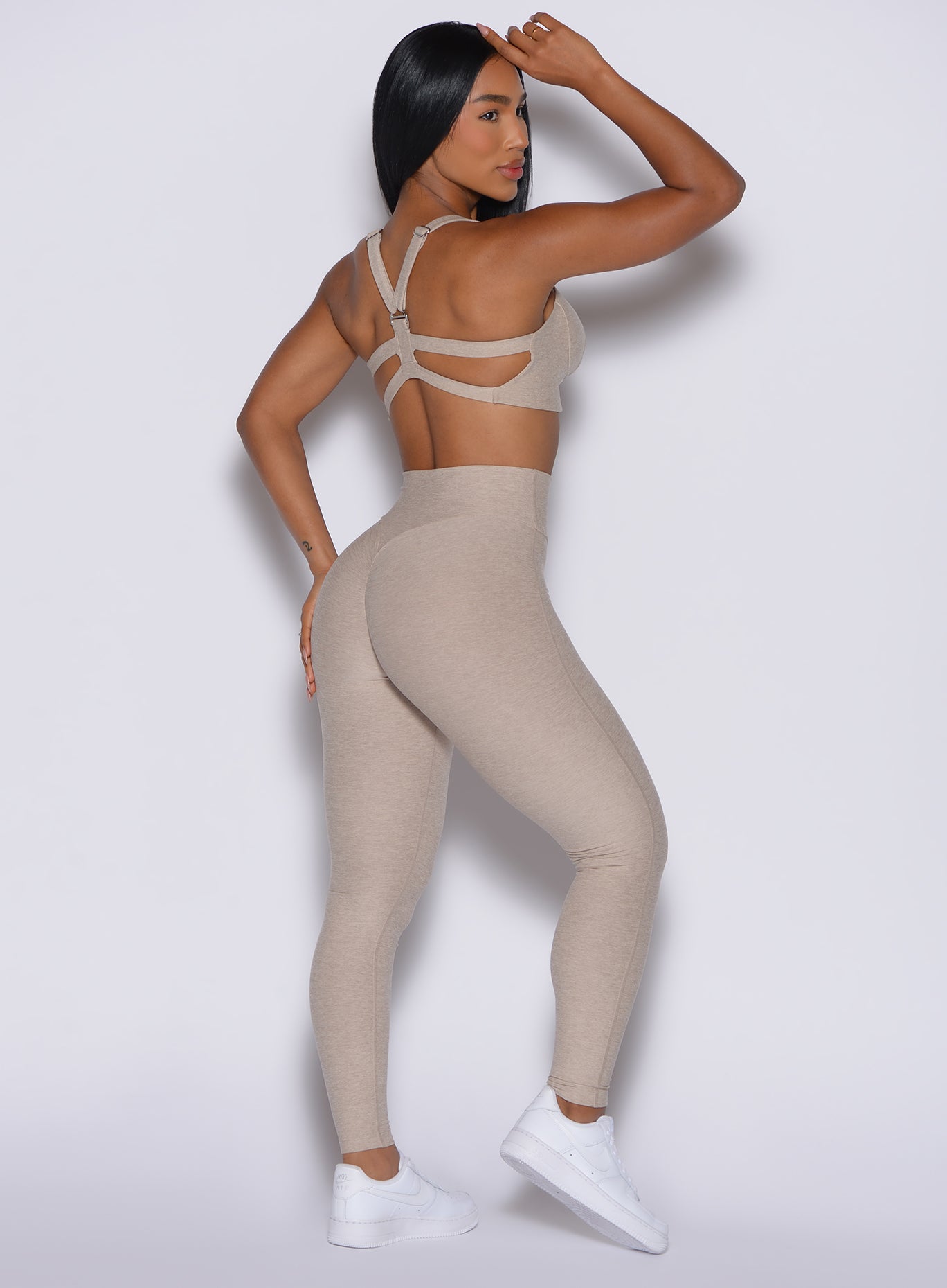 back profile of model angled to her right wearing the Movement Leggings in Taupe color and a matching Sports Bra 